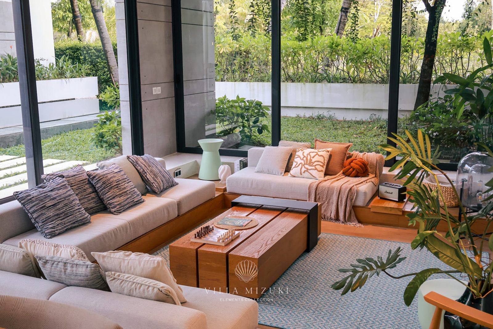 Bright and inviting seating area filled with natural light, accented by soft earth tones and tropical greenery outside the glass walls.
